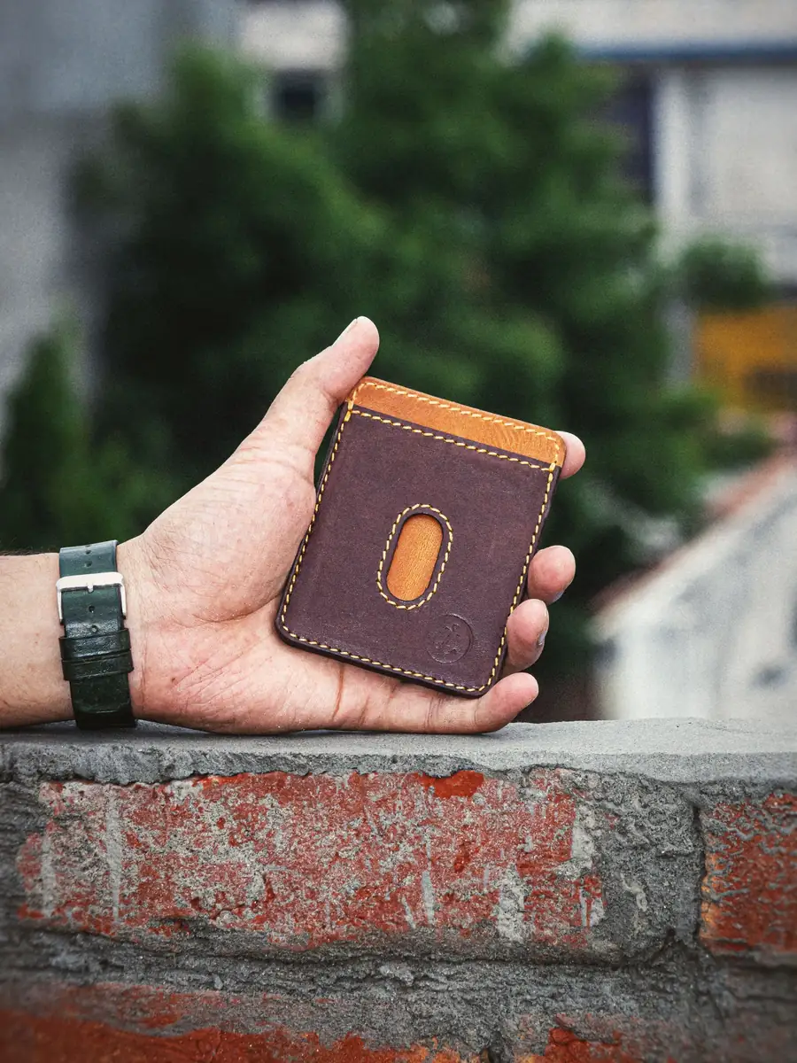 Hand holding a rugged brown leather wallet outdoors