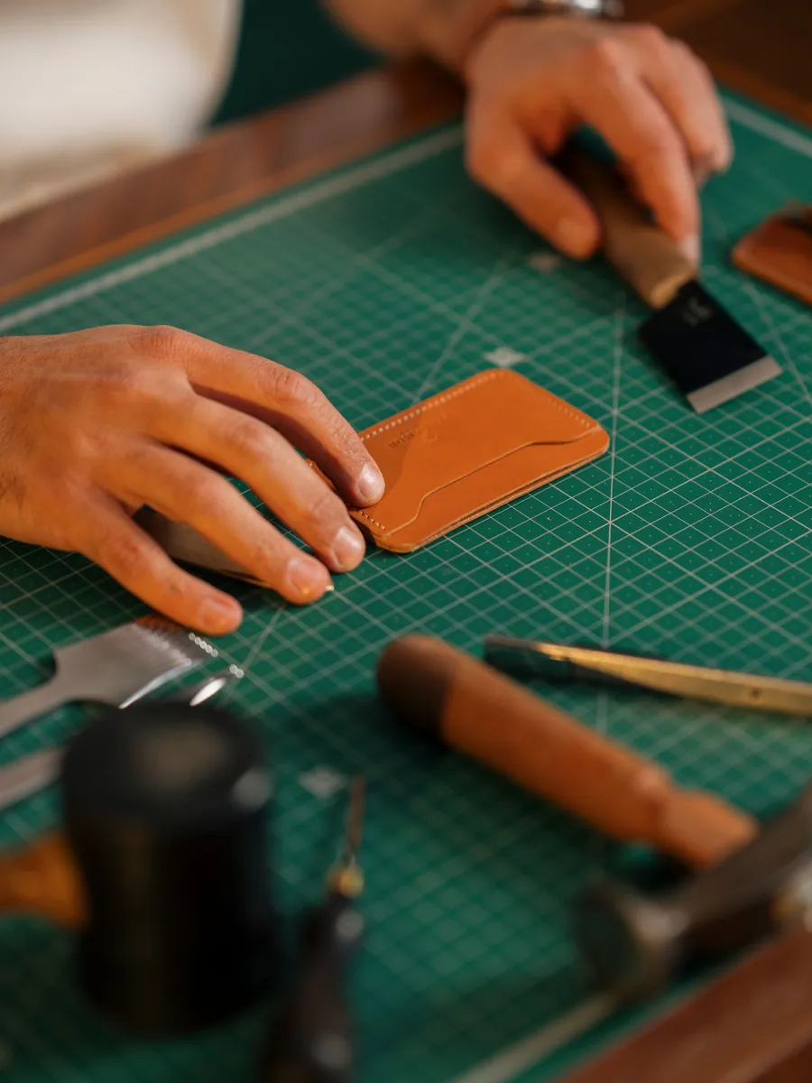 Hands assembling a leather wallet with precision tools