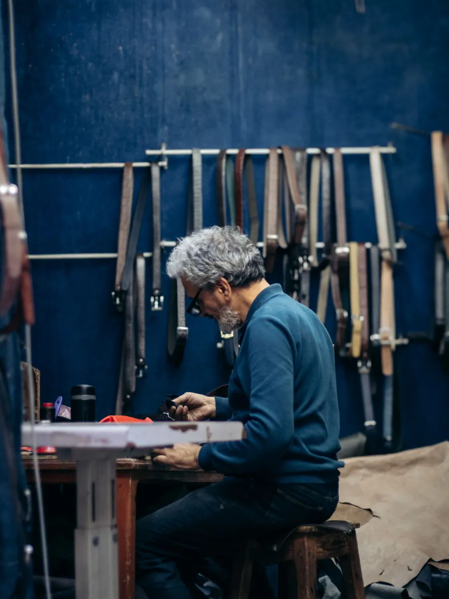Leather artisan shaping a belt at a tool-filled workbench