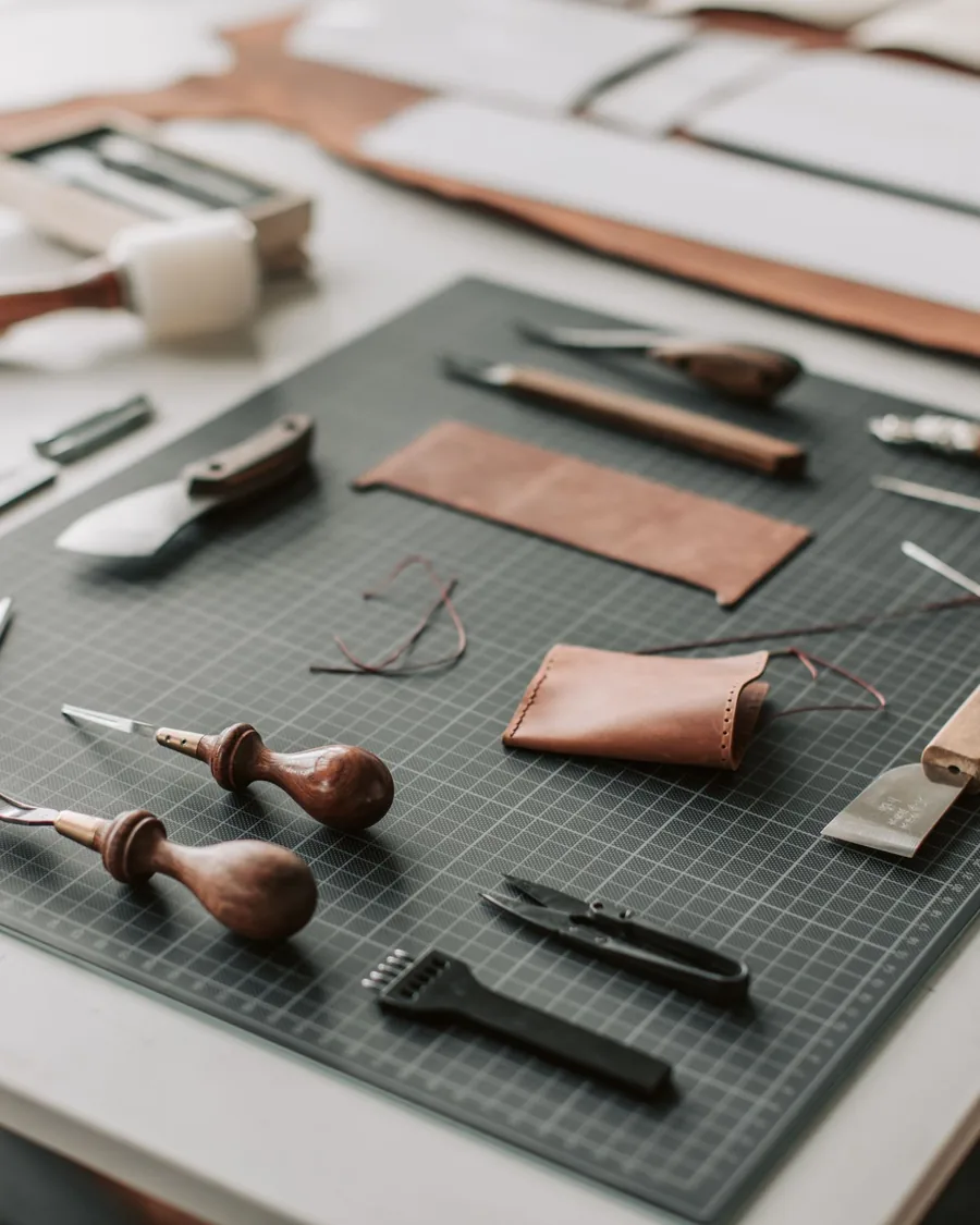 Leather knives, awls, thread, and hand tools on a cutting mat