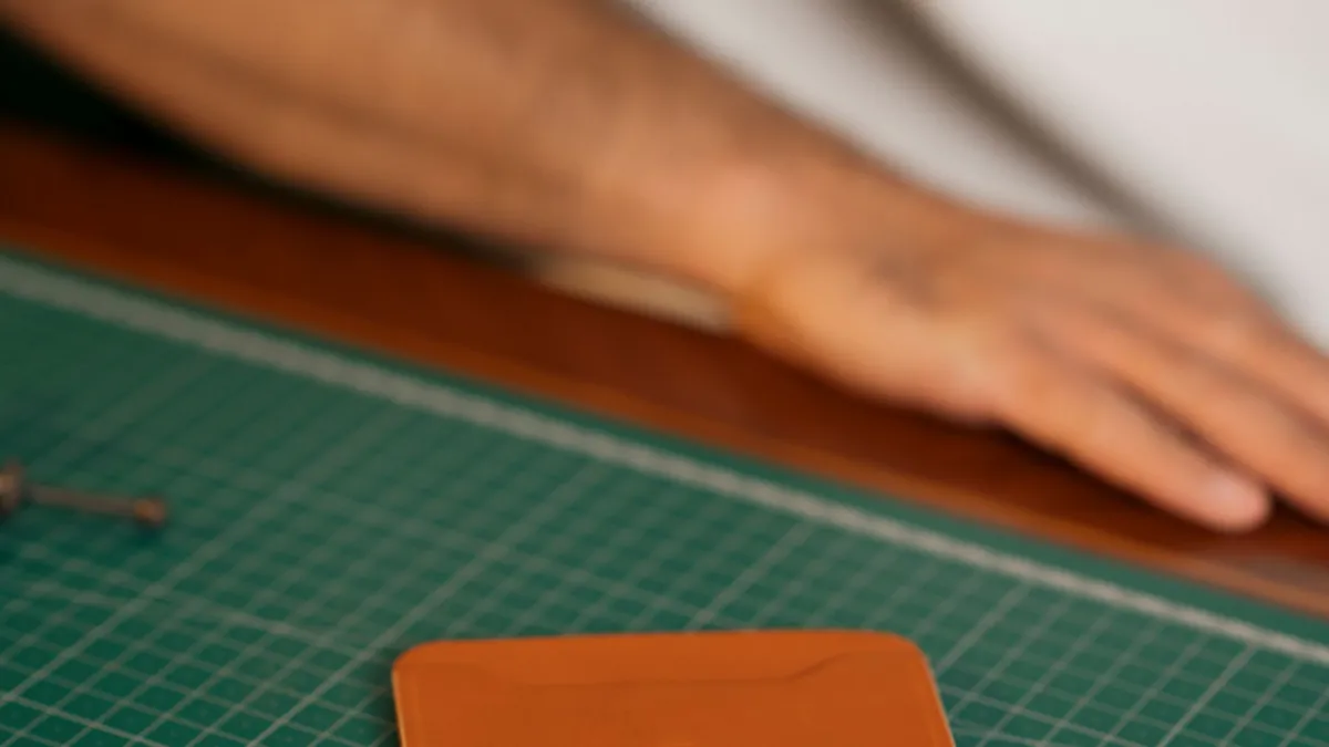Hands assembling a handcrafted leather wallet on a green mat